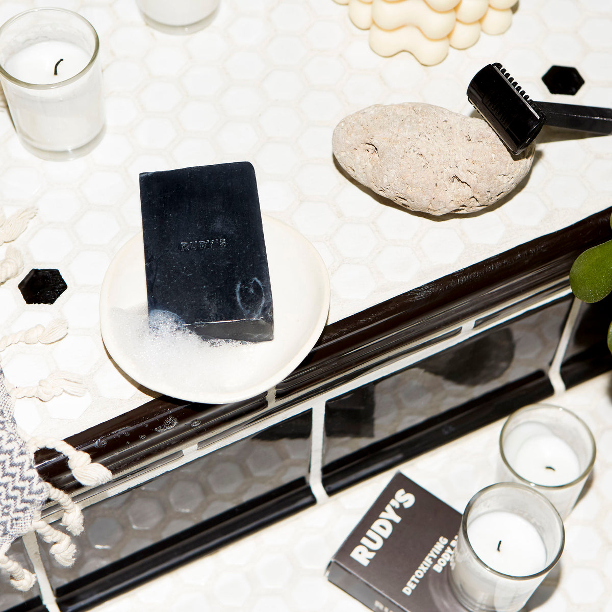 Bar of Black soap in dish on bathroom kitchen with candles and razor displayed around.