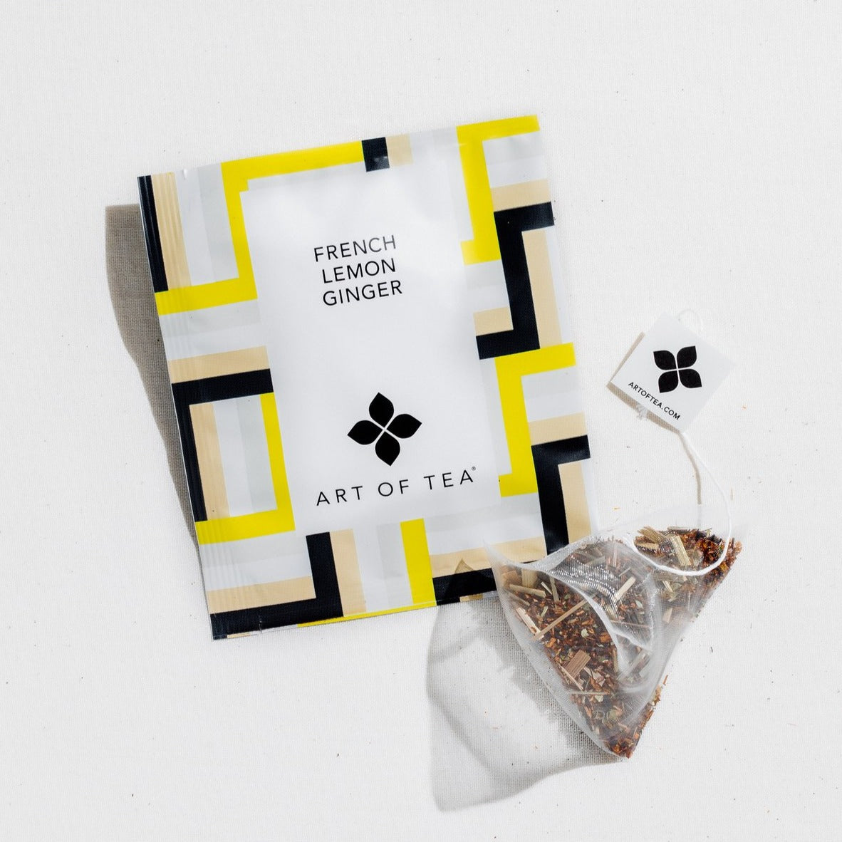 Square tea packaging with blue, tan, yellow and white square line design, with a tea sachet outside of the package to the right.