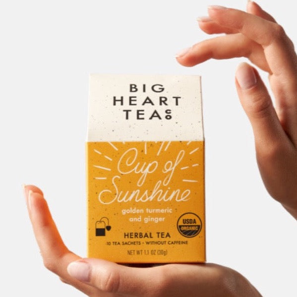 Yellow tea box packaging held by two hands on a white background.