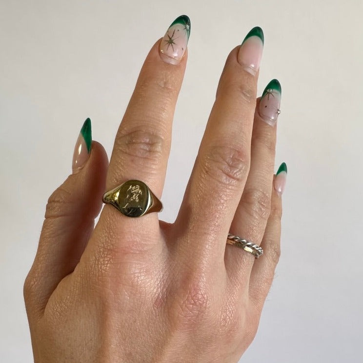 A woman&#39;s hand wearing a gold plated ring with an aquarius zodiac symbol engraved into the ring. She is wearing the ring on her right pointer finger