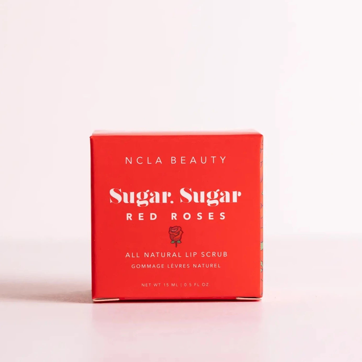 Red cube box packaging that has white text on the front that reads "NCLA Beauty Sugar, Sugar Red Roses. All Natural Lip Scrub". Cover has a small red rose illustrated under the name