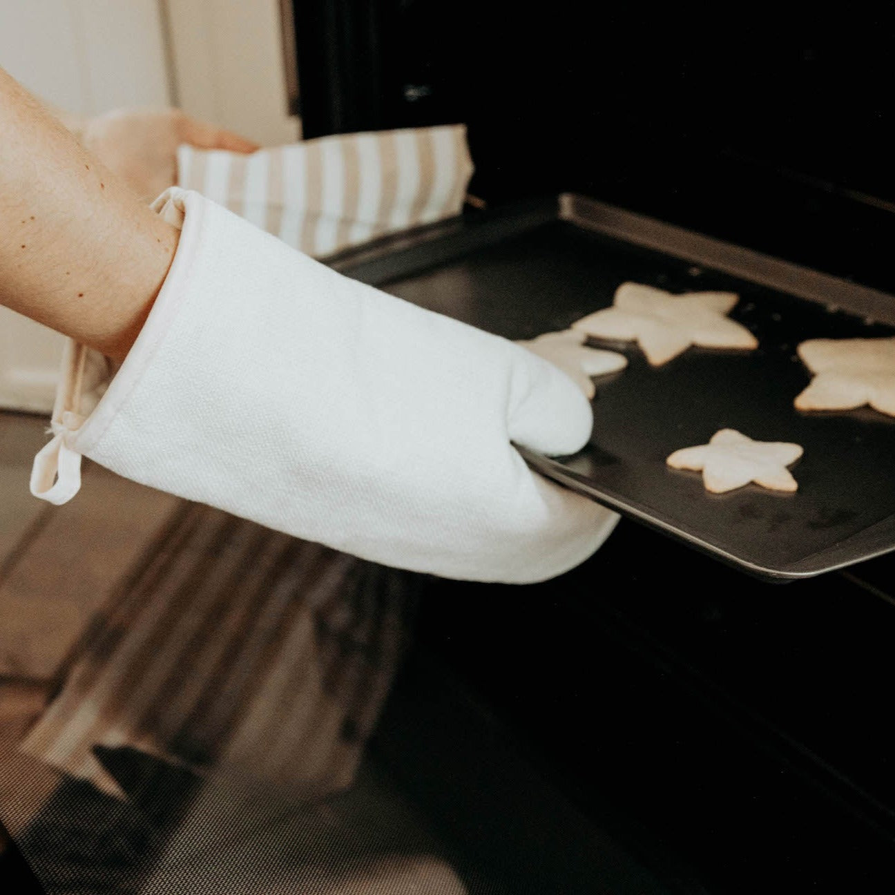 Oven mitt on hand as person takes tray of cookies out of the oven.