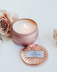 Pink sparking rose tin candle lit next to dusty pink roses.