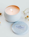 Lit Bourbon Vanille tin candle on white background with chamomile flowers surrounding.