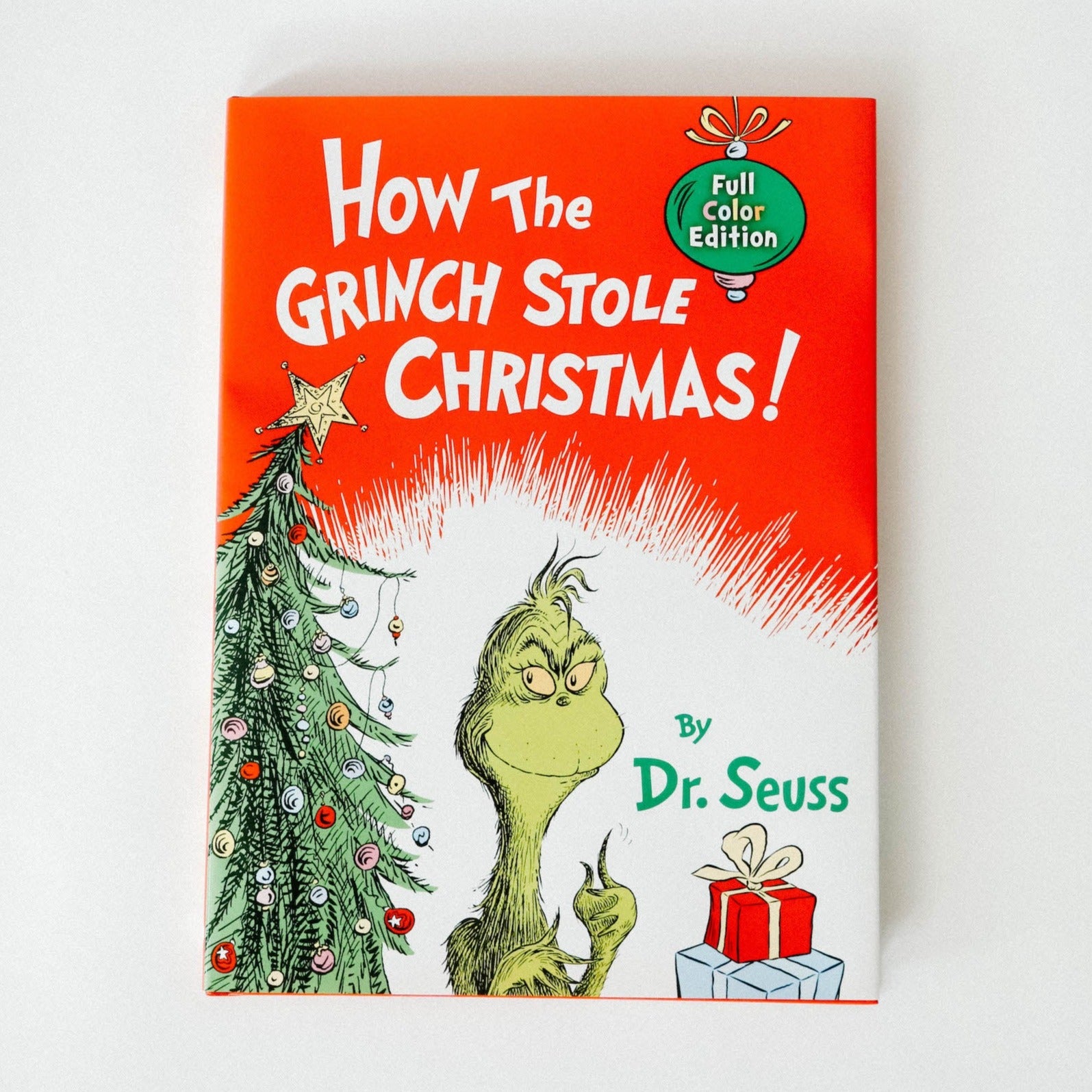 Hardcover of "How the Grinch Stole Christmas" 2021 book against a white background. The cover is red on top, white on the bottom with a cartoon decorated Christmas tree on the left, a cartoon grinch in the middle, and one blue and one red present on the right.