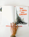 "How the Grinch Stole Christmas" opened up to the cover page, which is white on the left and has a cartoon Christmas tree and the title of the book in red on the right.