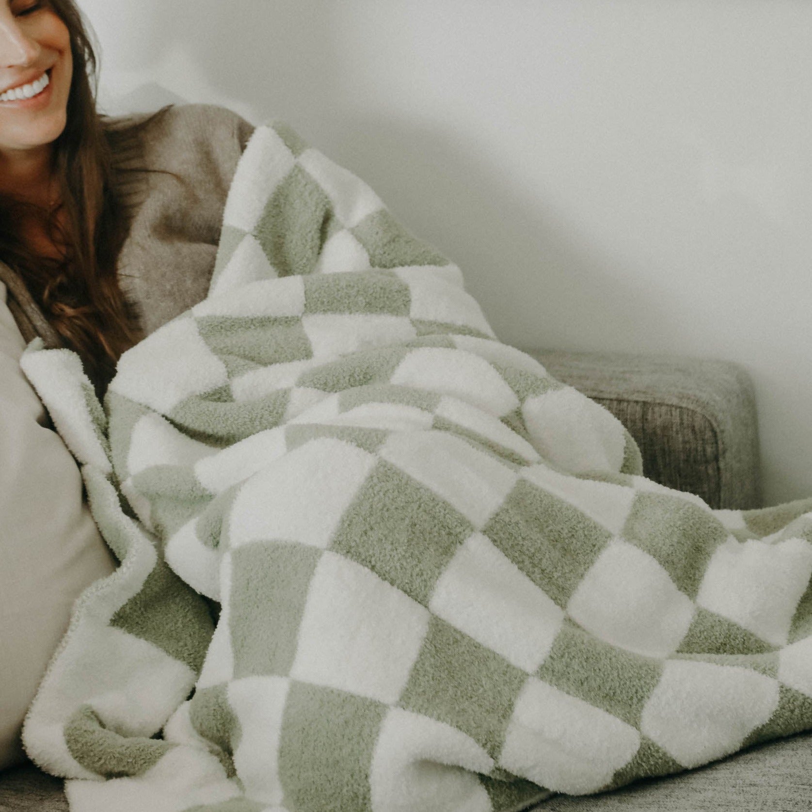 A brunette girl laying on a couch with a green checkered plush blanket wrapped around her.