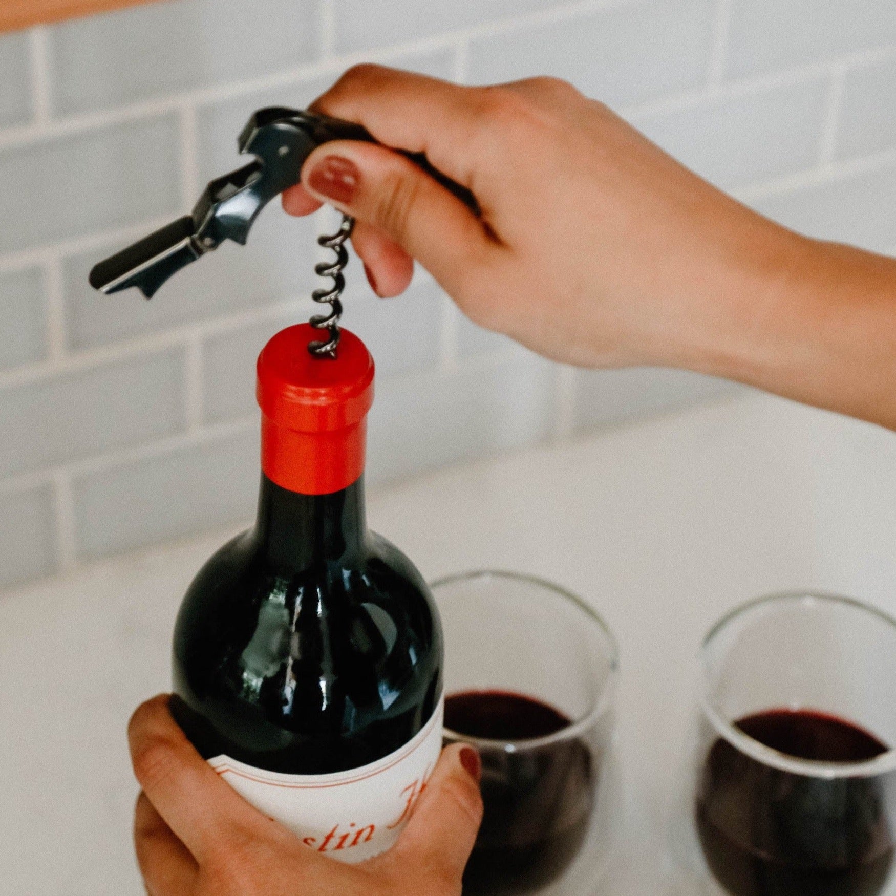 A black wine opener being used to open a bottle of red wine..