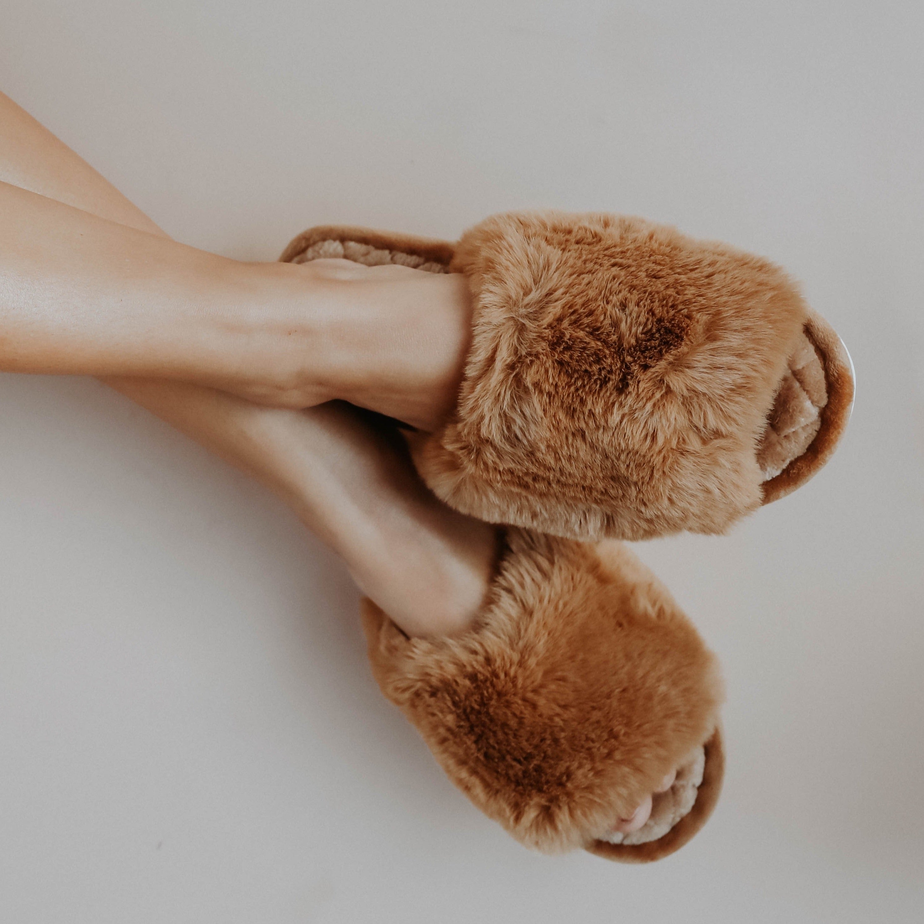 A girl crossing her legs wearing brown fuzzy slippers against a white background
