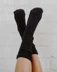 A girl with tan legs wearing mid-calf navy blue fuzzy socks with her legs up in the air criss-crossing against a white background