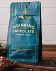 Navy blue bag for Drinking Chocolate. has cold accents  and white text. Bag is on wooden table with wooden spoon full of the drinking chocolate 