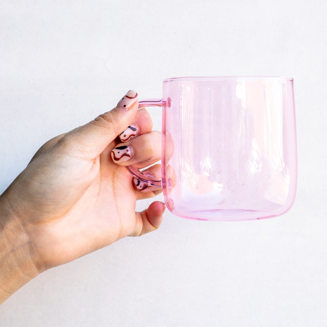 Hand holding empty pink glass mug.