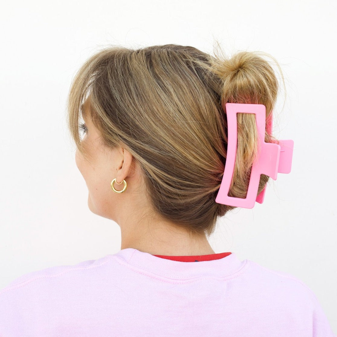 A girl with blonde hair in an updo wearing an XL matte baby pink claw clip against a white background.