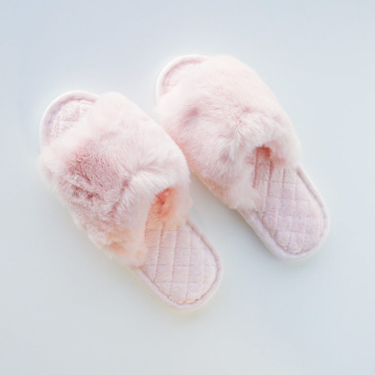 A pair of light pink fuzzy slippers on a white background.