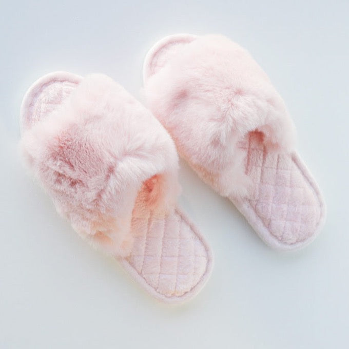 A pair of light pink fuzzy slippers on a white background.