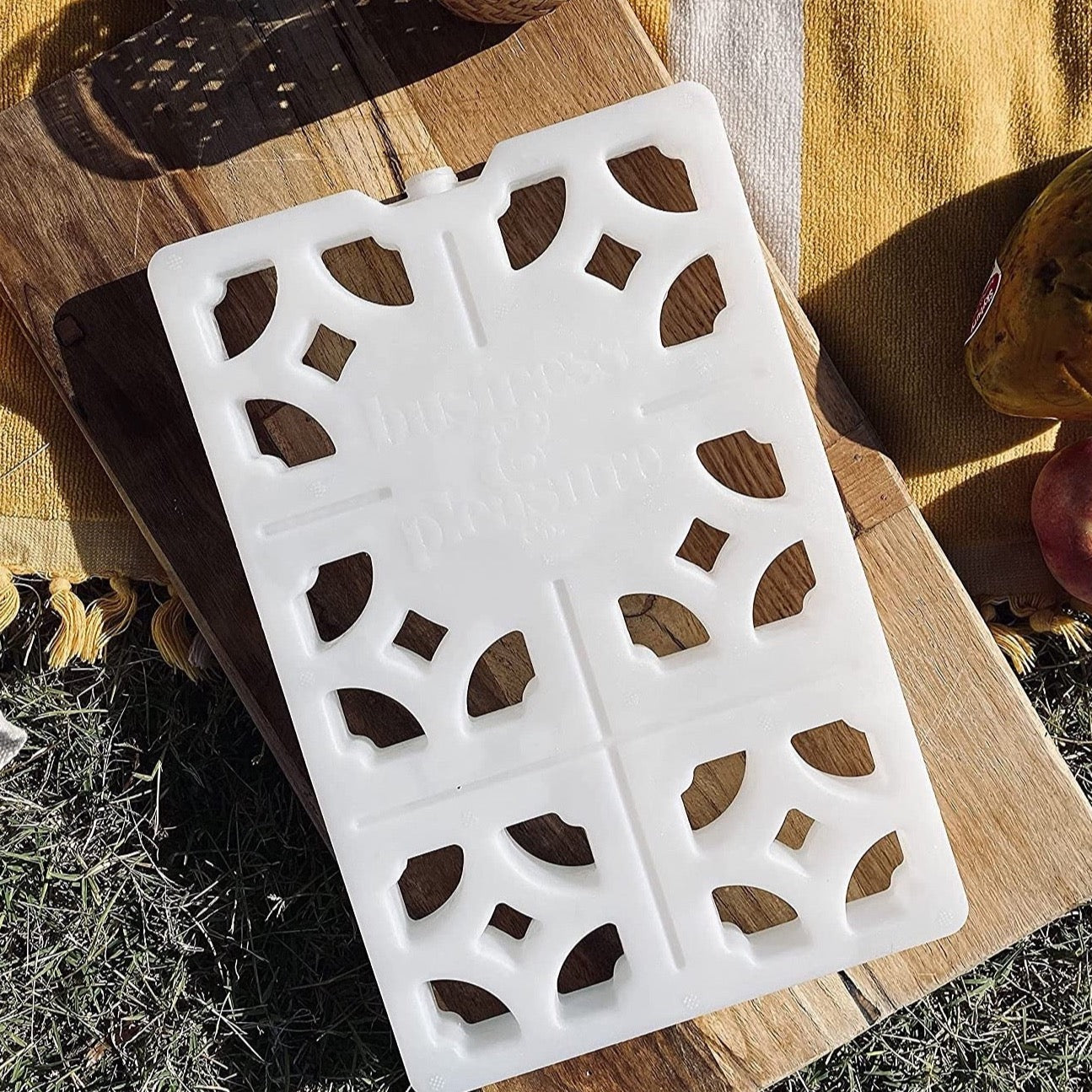 white breeze block ice pack on piece of wood in a picnic setting. Ice pack has cut outs resembling mosaic pattern