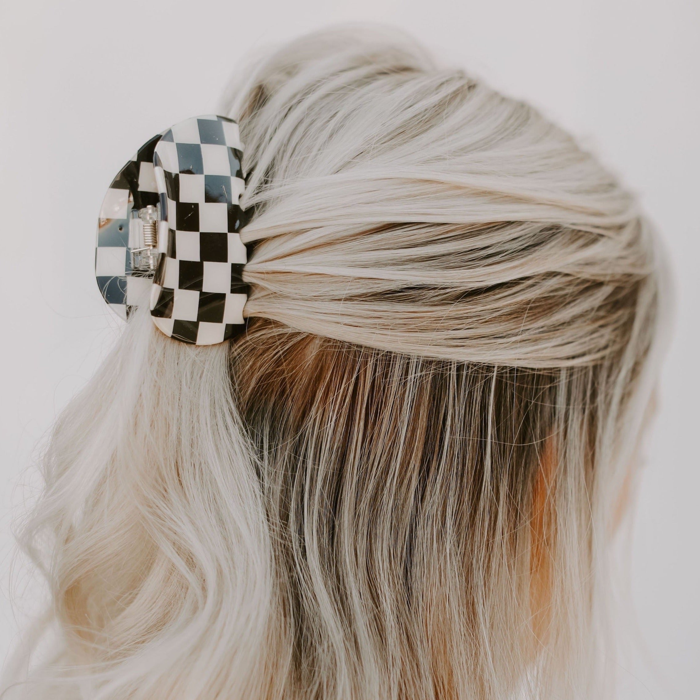 Blonde Haired female with black and white checkered hair clip pulling hair half up.