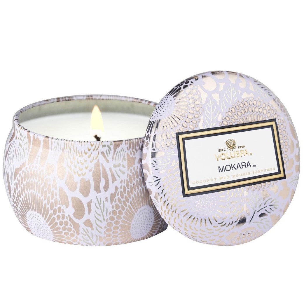 Mokara candle in silver tin with floral detail, with lid leaning against it.