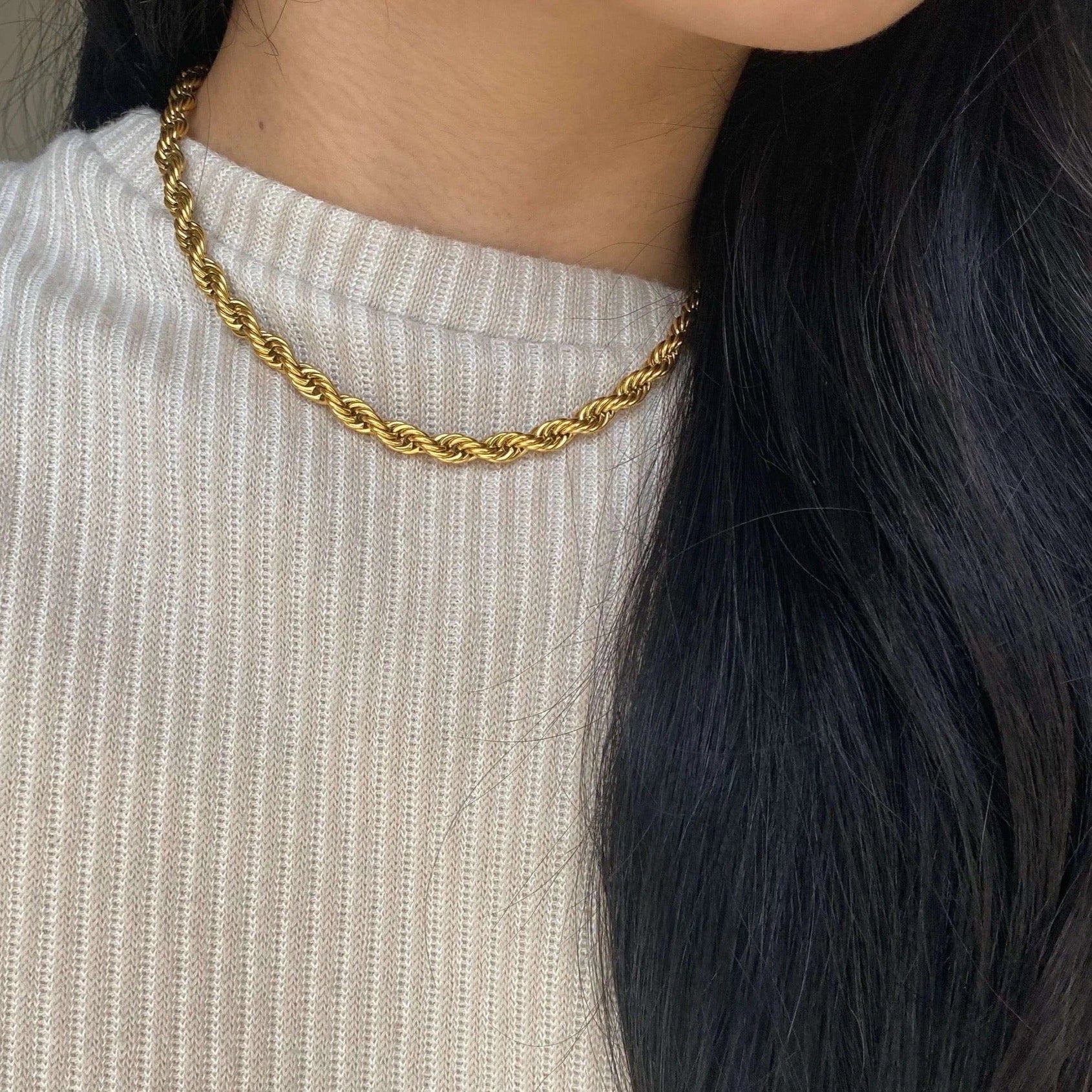 Girl with dark brow hair wearing a white sweater and a twisted gold chain necklace