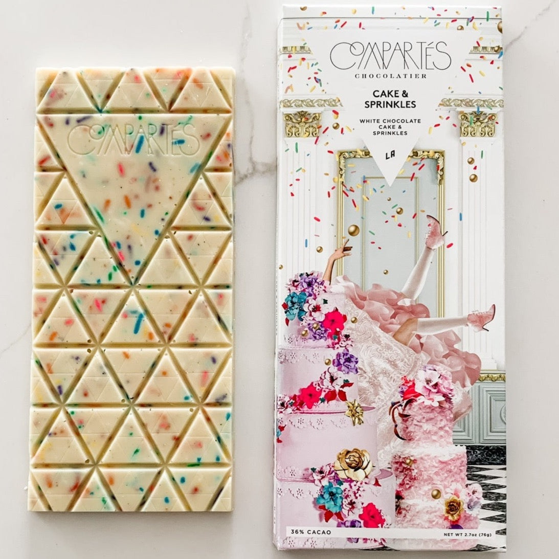 White chocolate bar with sprinkles next to packaging featuring ornate cake with woman stuck in it.