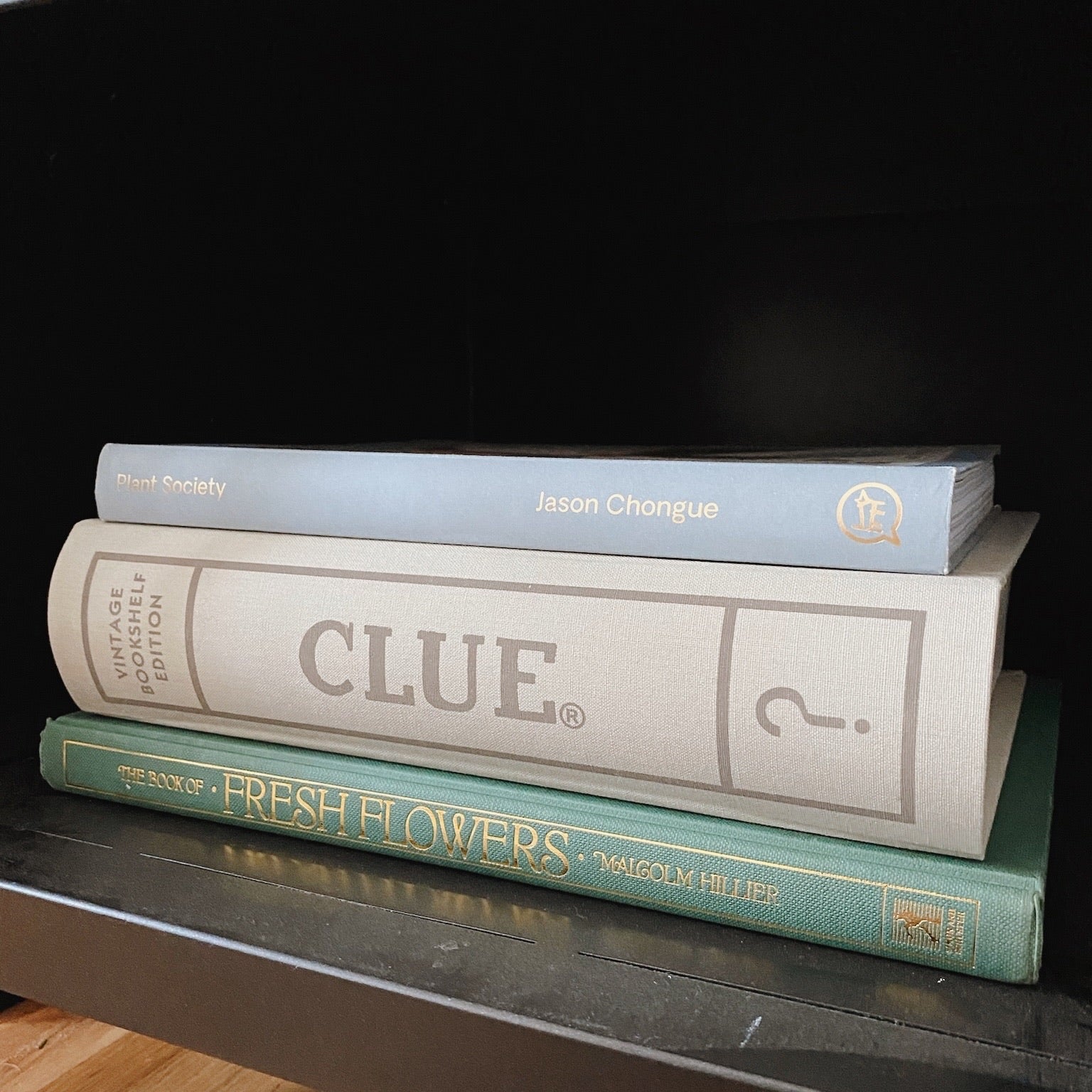 Linen Clue Board Game displayed on black bookshelf in stack of books.