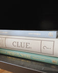 Linen Clue Board Game displayed on black bookshelf in stack of books.