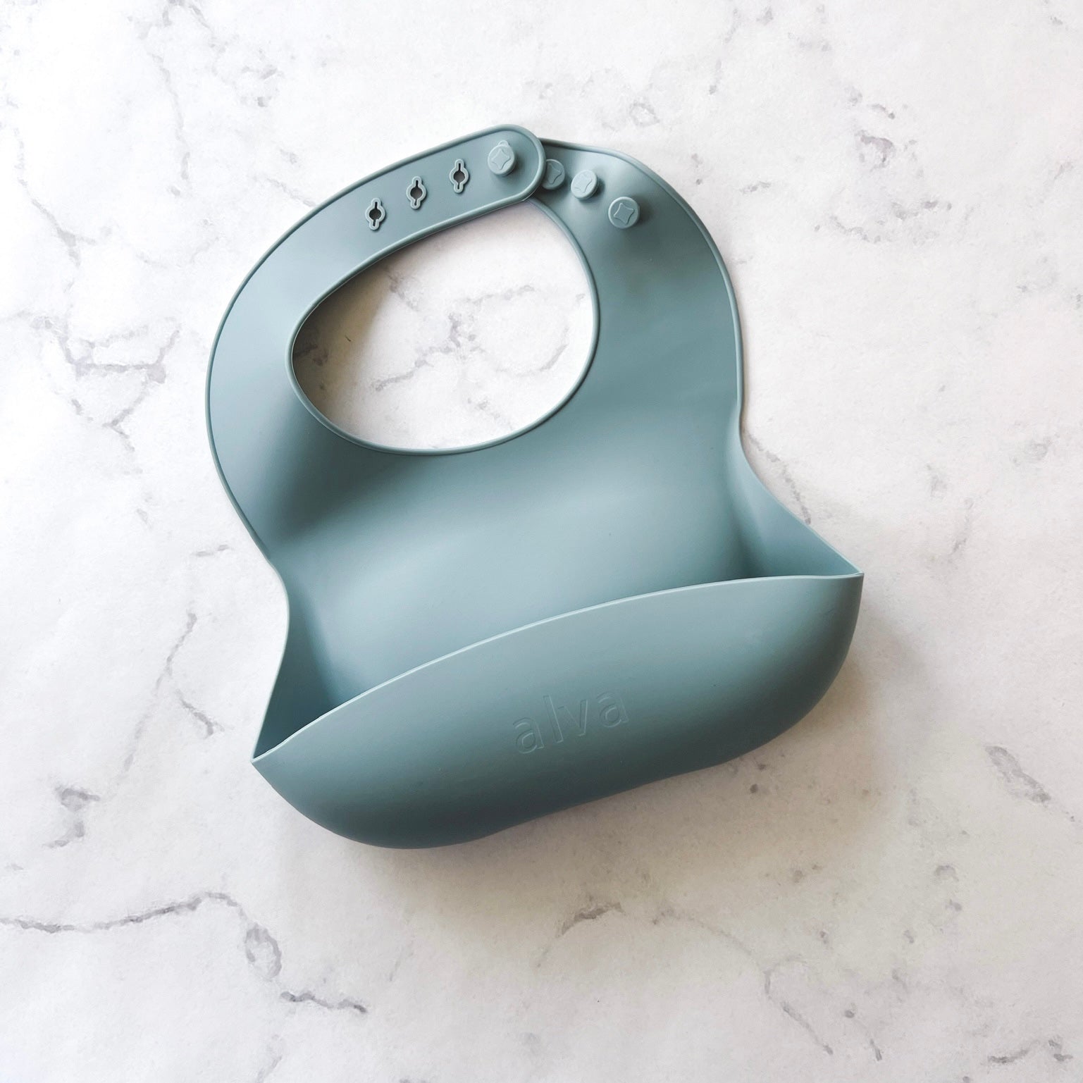 Alva blue silicone baby bib against a white marbled table