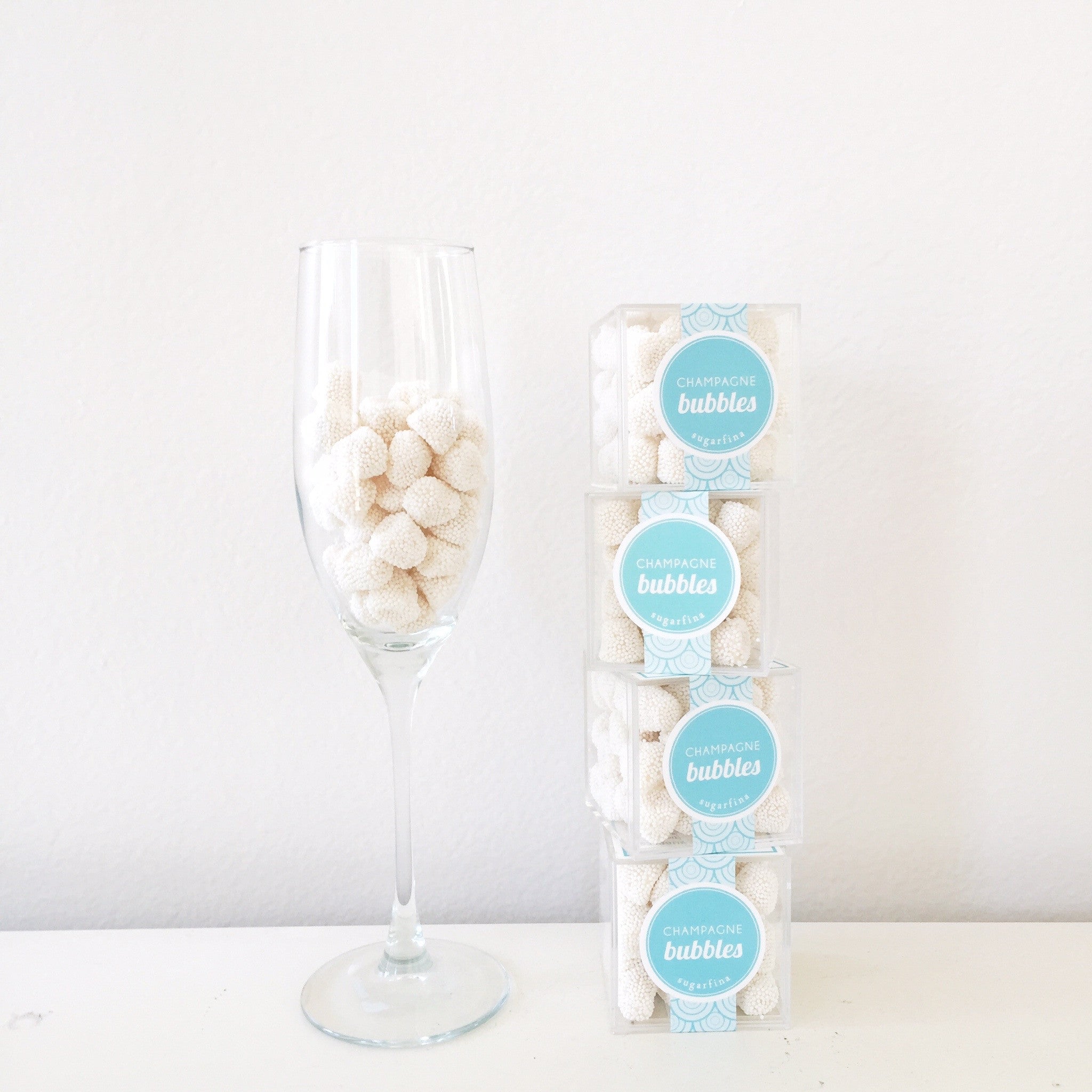 Stack of four Sugarfina Celebratory Champagne Bubbles cubes to the right and a champagne flute filled with the champagne bubbles to the left.