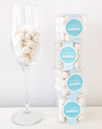 Stack of four Sugarfina Celebratory Champagne Bubbles cubes to the right and a champagne flute filled with the champagne bubbles to the left.