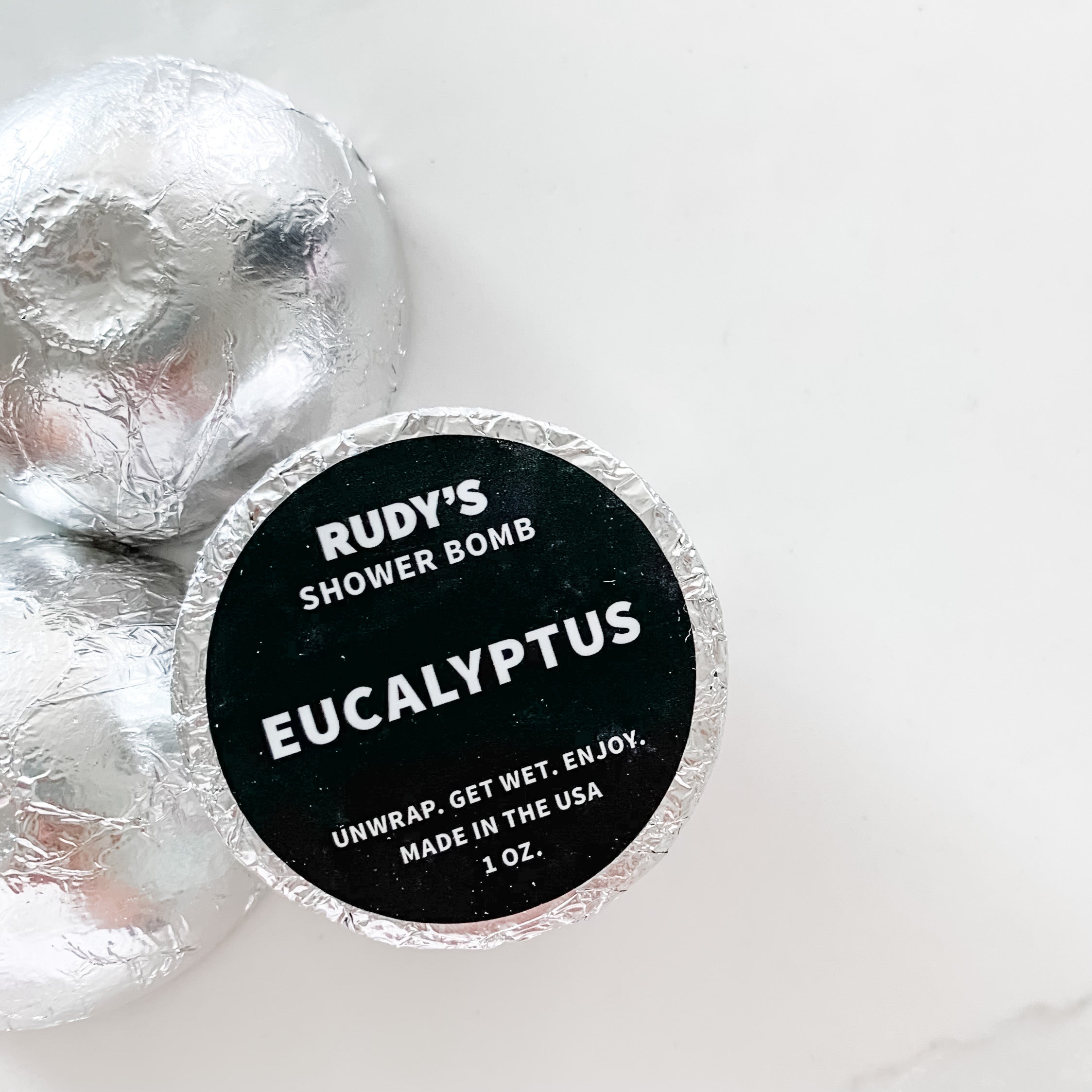 Three Rudy's shower bomb in silver foil packaging with black sticker shown on one.
