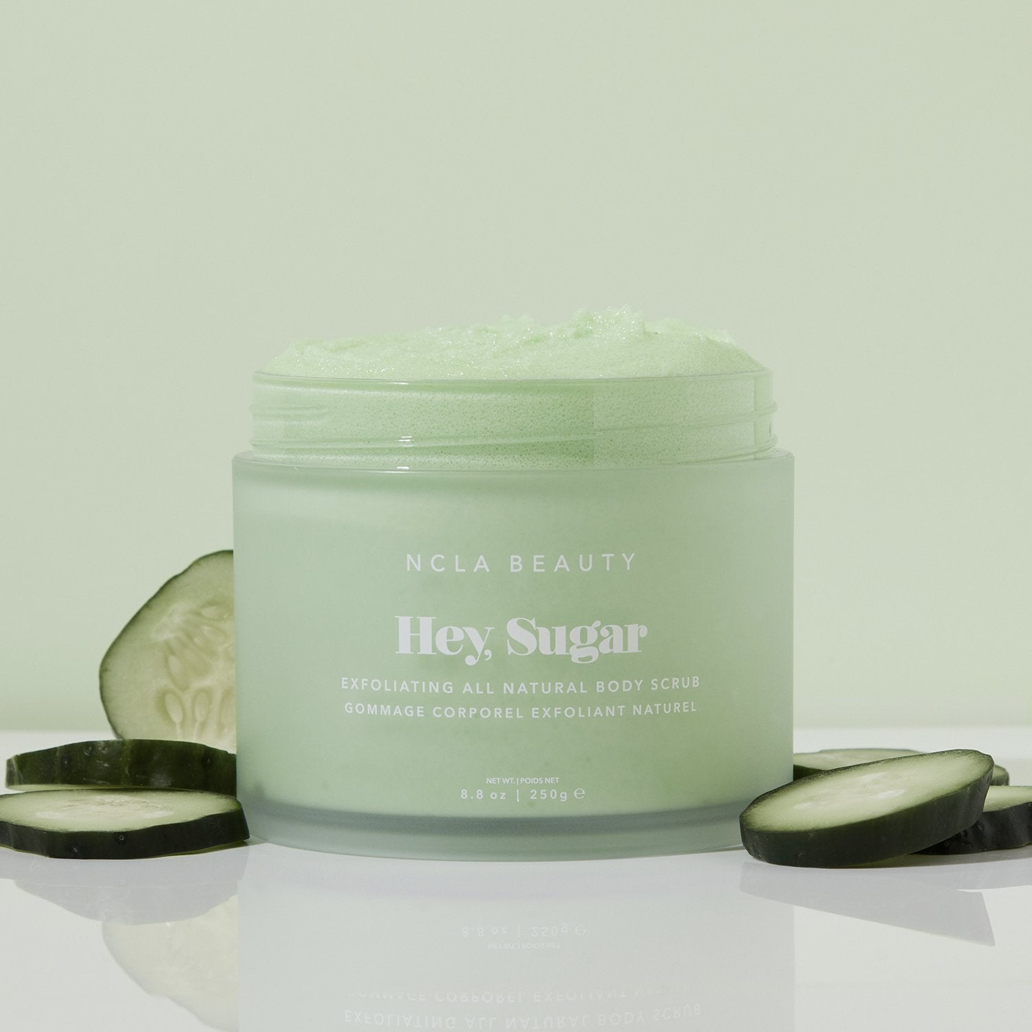 Cucumber sugar scrub in clear packaging, surrounded by cucumber slices.