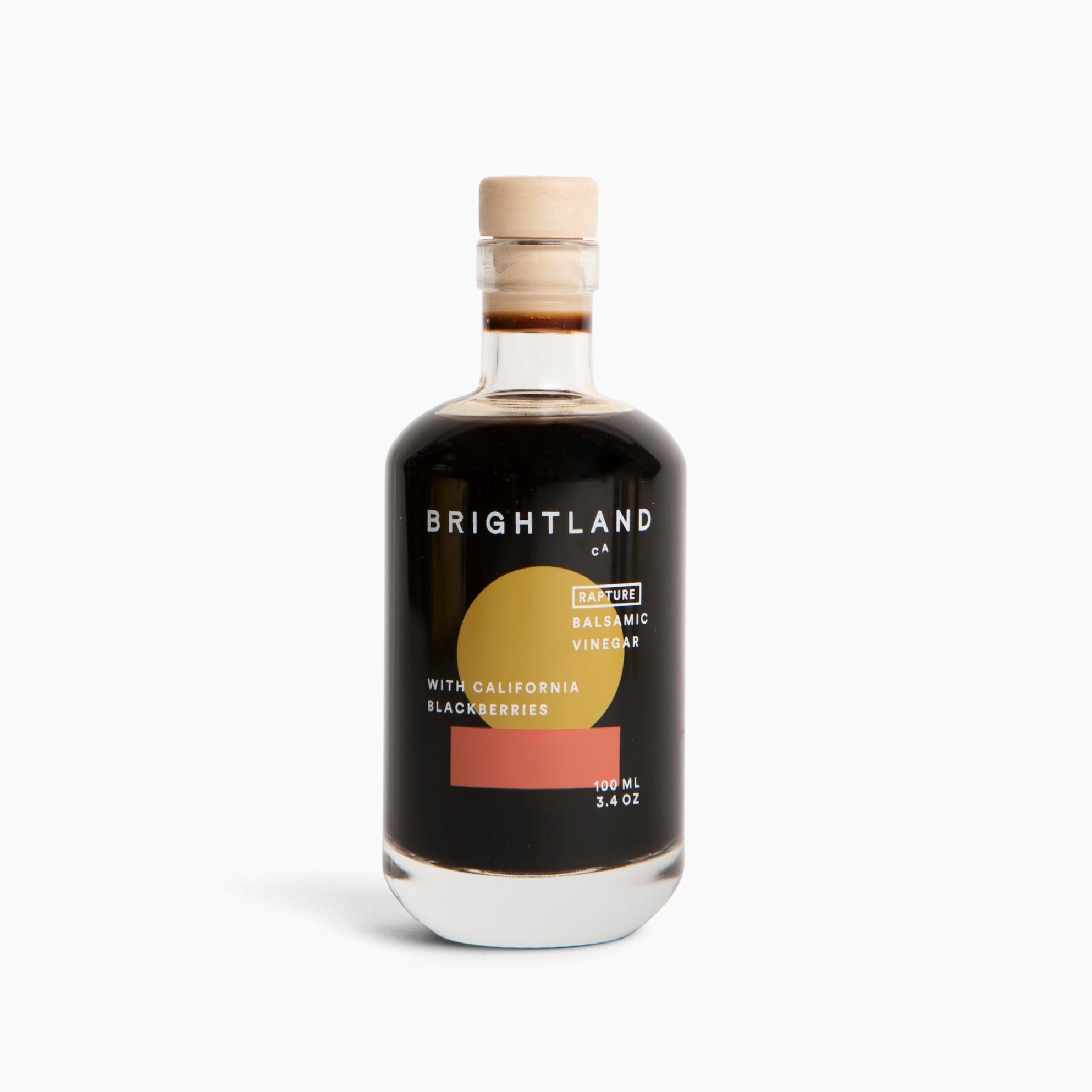 A glass bottle with beige cork topper containing dark brown vinegar. White Text on bottle reads, "Brightland CA Rapture Balsamic Vinegar With California Blackberries 200mL 3.4 oz". Photographed on white background. 