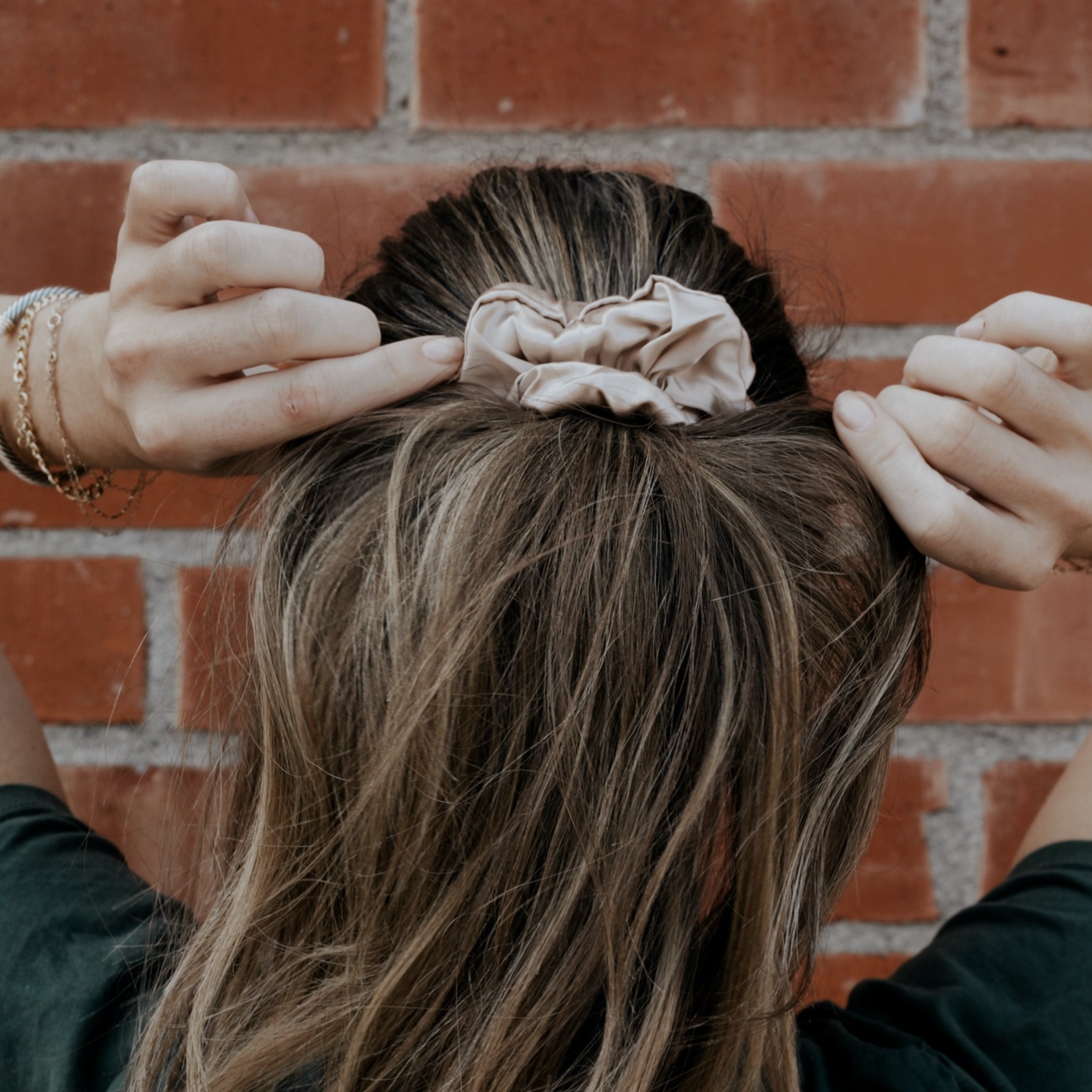 Girl tightens ponytail that is secured with champagne thick scrunchie.