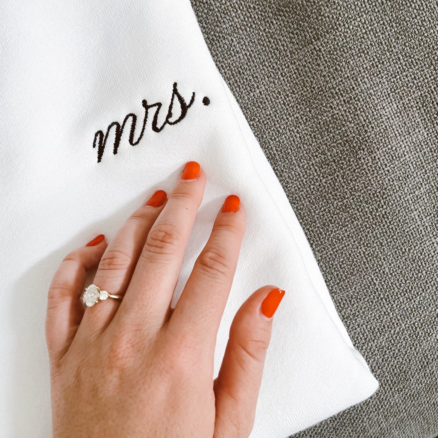 Hand with engagement ring resting on white Mrs. sweatshirt.