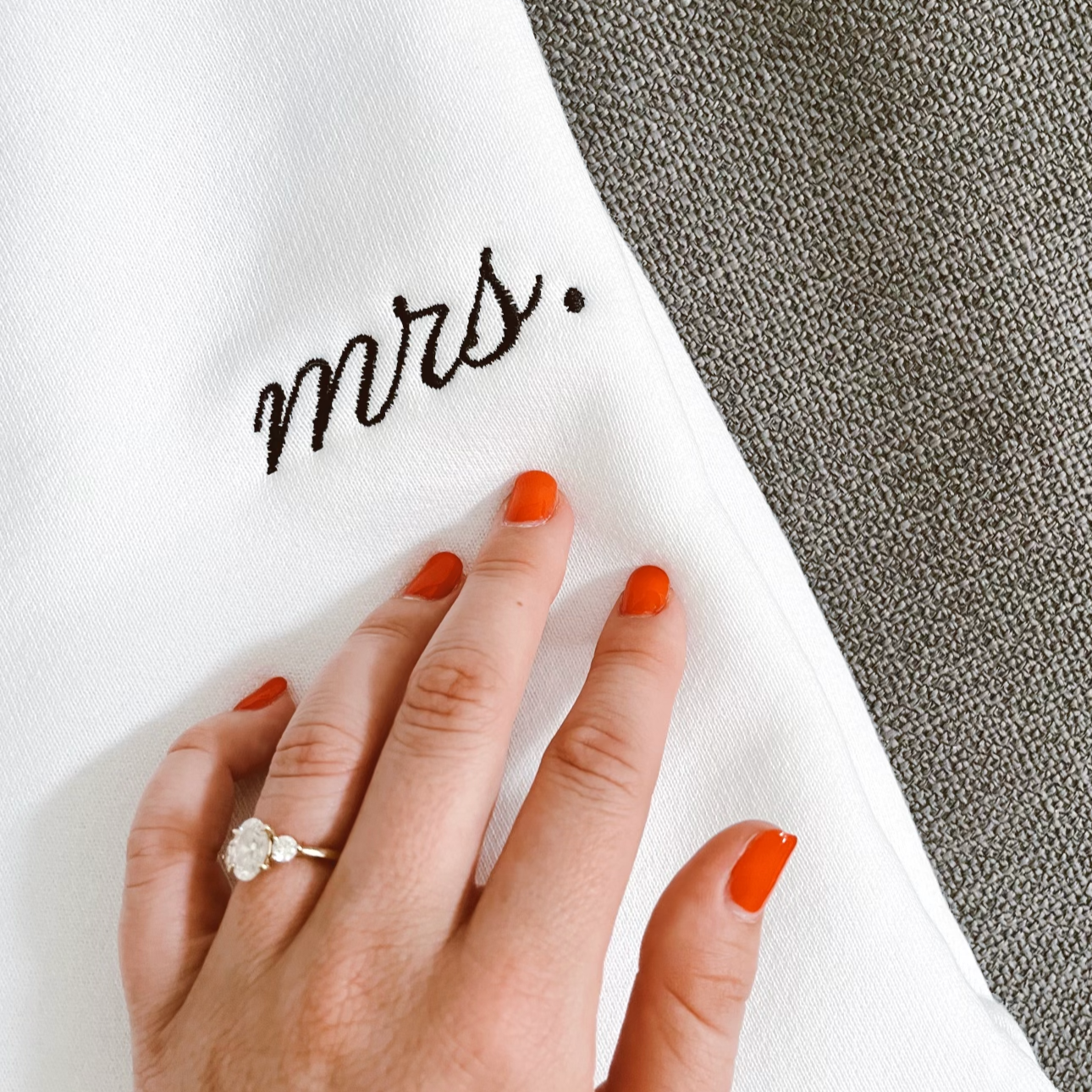 Hand with engagement ring rests on white Mrs. sweatshirt.