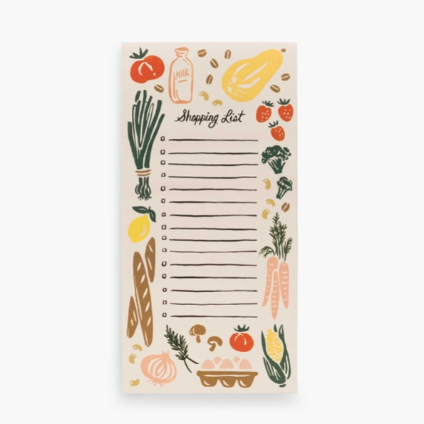 Beige colored note pad with "Shopping List" in black cursive text on top with colorful produce depictions around edges. Photographed against white background.