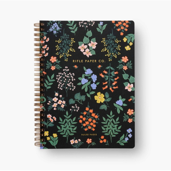 Black notebook with gold spiral binding with multicolor floral artwork on front. Photographed on white background.