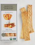 A box of the Rustic Bakery Olive Oil & Sel Gris Organic Sourdough Flatbreads laying to the right of 4 flatbread crackers. Photographed on light grey background.