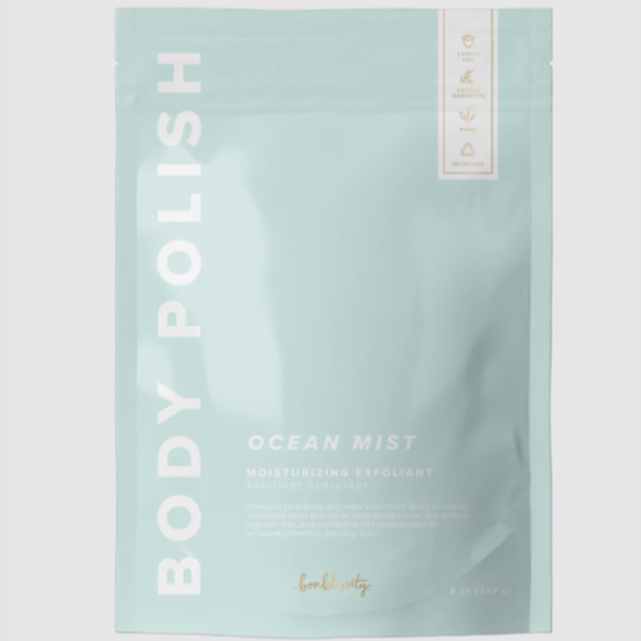 Rectangular, sealed, light blue plastic bag with white text that reads "BODY POLISH" on the side and "OCEAN MIST MOISTURIZING EXFOLIANT" in bottom right. Photographed on grey background. 
