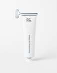 A white squeeze tube with silver rolling dispenser at tup. Black text on tube reads, "Act+Acre Restorative Hair Mask". Photographed on white background. 