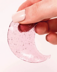 A caucasian hand with beige painted nails holding a single Rosé Hydrating Under Eye Gel. Photographed on white background.