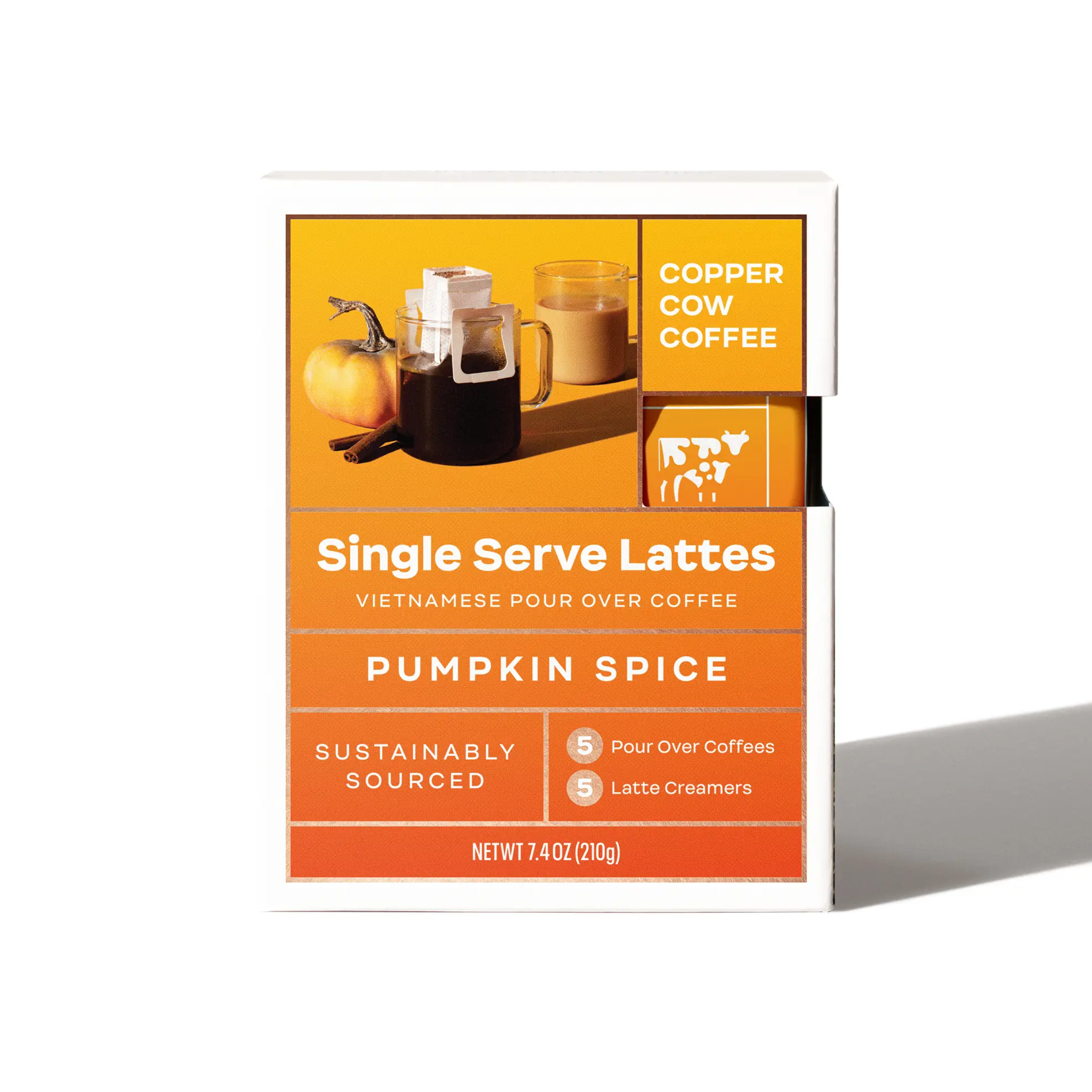 A square box with yellow to deep orange gradient and picture of pour over tablescape in top right with a small pumpkin, clear coffee mug with pour over filter on top, and a clear coffee mug with a latte. Text on box reads, "Copper Cow Coffee Single Serve Lattes Vietnamese Pour Over Coffee Pumpkin Spice Sustainably Sourced 5 Pour Over Coffees 5 Latte Creamers Net Wt 7.4 OZ (210g). Photographed on white background. 