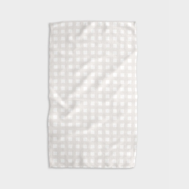 A white tea towel with beige grid design folded into a rectangle and photographed on white background.