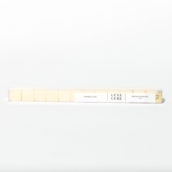 A long, clear rectangular tube filled with light yellow/ orange sugar cubes. White label on far right end of tube reads, &quot;Mimosa Cube | LUXE CUBE | Arcadia Orange 1.7 oz&quot;. Photographed on white background. 