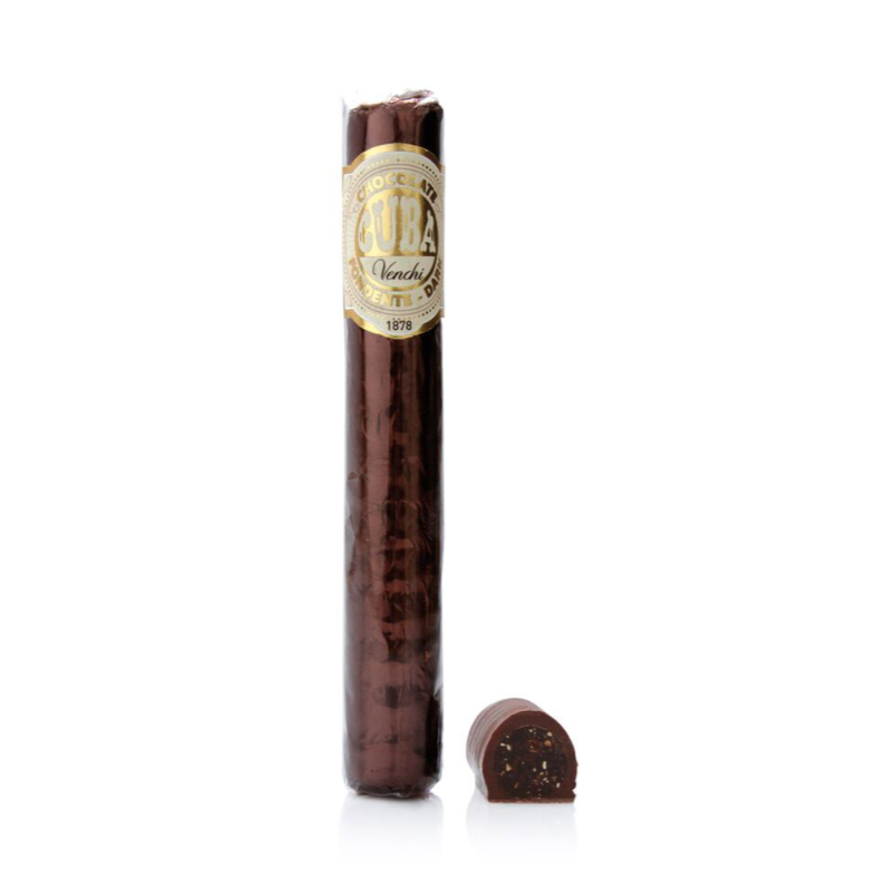 A cigar shaped chocolate wrapped in cellophane packaging and and cigar-like label that reads &quot;Chocolate CUBA Venchi&quot; next to a cut piece of chocolate cigar showing fondant and hazelnut filling dipped in dark chocolate. 