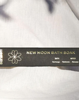 A black rectangular box with gold writing that reads, "Ollie Blossom New Moon Bath Soak Bath Notes Recharge, Meditate, Release" photographed on white linen.