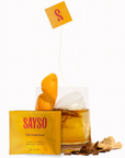 Image shows the SAYSO Old Fashioned Ready-to-make cocktail sachet in the forefront of the image, with an Old Fashioned made cocktail towards the back. There is an unpackaged sachet in the drink, as well as some of the ingredients surrounding it.
