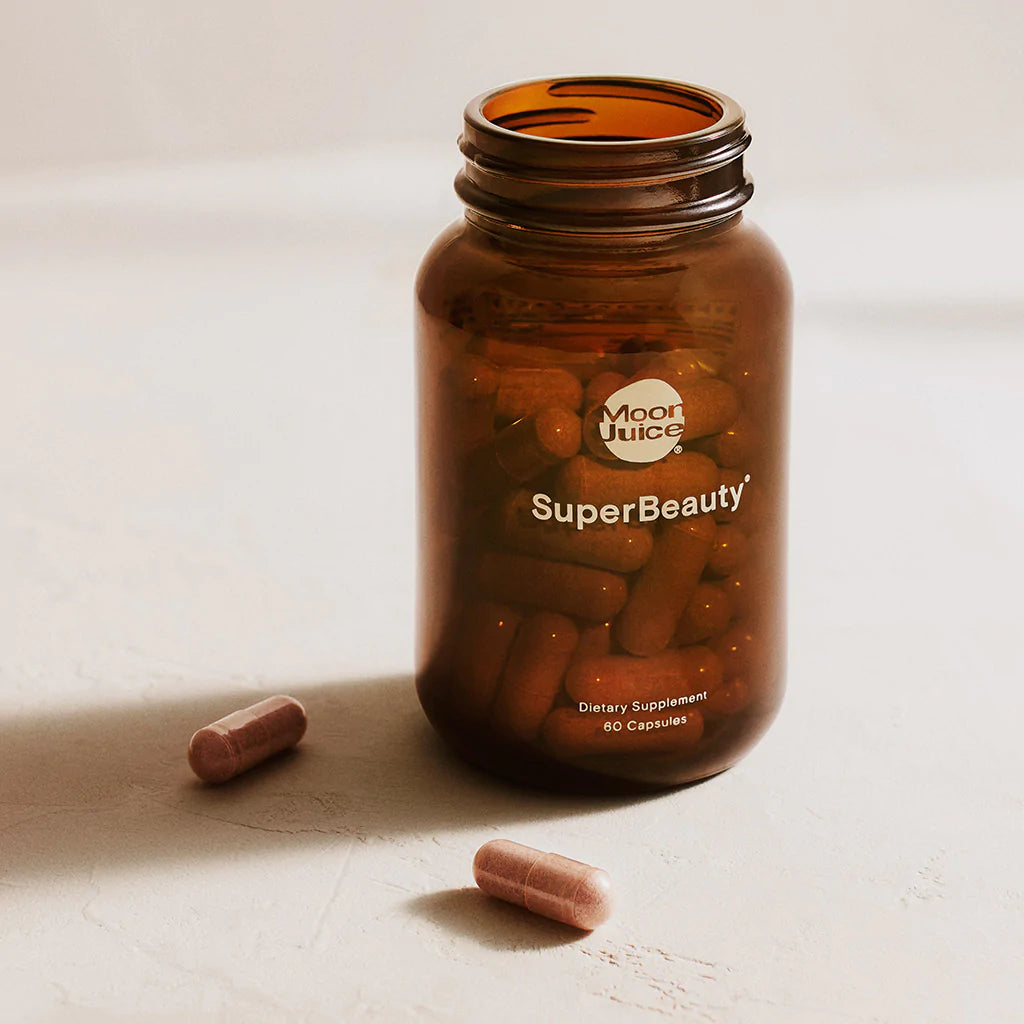 Open brown bottle of Moon Juice SuperBeauty capsules with two capsules beside the bottle.
