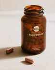 Open brown bottle of Moon Juice SuperBeauty capsules with two capsules beside the bottle.