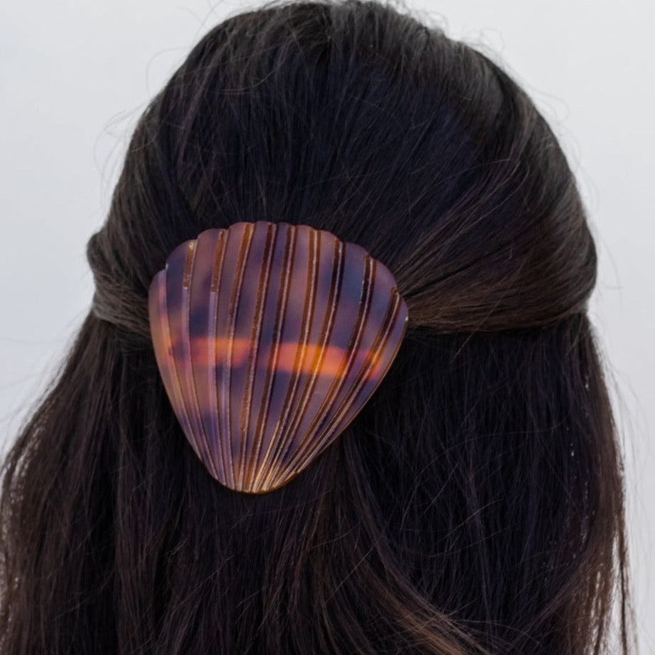 Girl with dark brown hear wearing a brown tortoise seashell hair clip with her hair half up, against a white background
